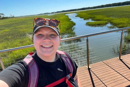 A person stands on a bridge in front of a marsh.