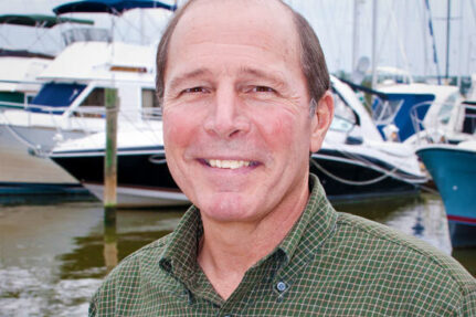 Nick stands on a dock with boats in the background.