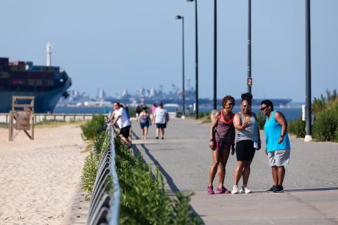 Three women stop to take a photo along a boardwalk near a beach.