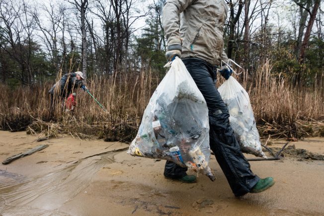 Person carries two bags filled with trash away from a beach.