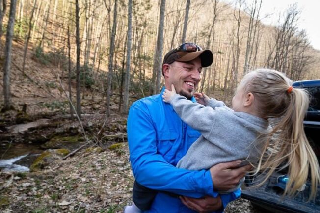 Dustin Wichterman holds his daughter as they stand by a trout stream.