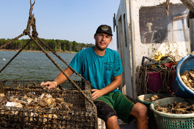 Oyster farmer Jerry Sturmer sits on his boat between the cabin and a cage full of oysters.