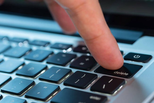 Finger touching delete button on a keyboard.