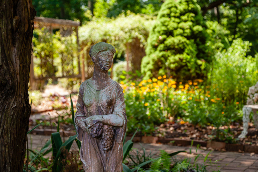 A white stone goddess is focused with bright yellow flowers and green shrubs filling the background