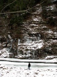 A photo of a lone dark figure on snow in front of a tall, rocky waterfall