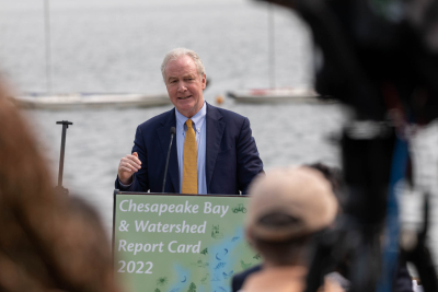 Senator Chris Van Hollen stands at a podium in front of water with people listening in front