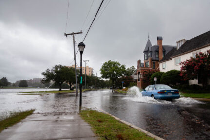 Blue car drives through a heavily flooded street.