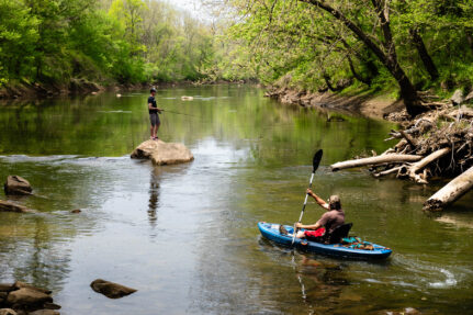 Dennis Radigan of Aberdeen, Maryland, paddles his kayak into Deer Creek at Susquehanna State Park in Harford County, Maryland, while a man fishes from a nearby rock.