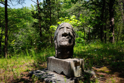 Sculpture of a large face made out of limestone rock surrounded by grass and trees.