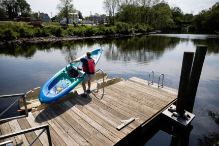 A paddler carries a kayak to an accessible launch overlooking a creek