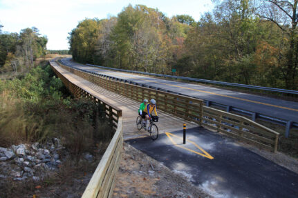 Two cyclists exit a bridge over a large stream or river.