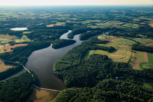 Aerial of the water with surrounding forest and farmland.