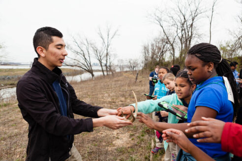 Teacher shows antlers to students by a stream in winter.