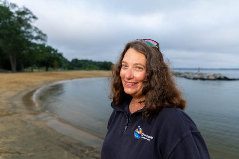 Jody, a white woman with brown hair, stands in front of a beach.