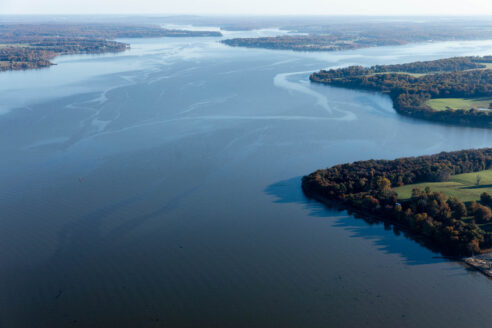 An aerial view of a wide blue river with a forested shoreline.