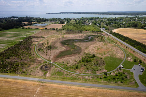 Aerial view of park with trees and circular trail and river in the background.