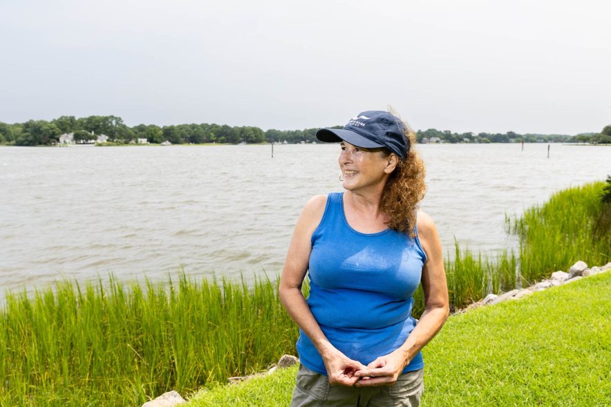 Marie is a white woman wearing a blue shirt and blue hat, standing in front of the river.