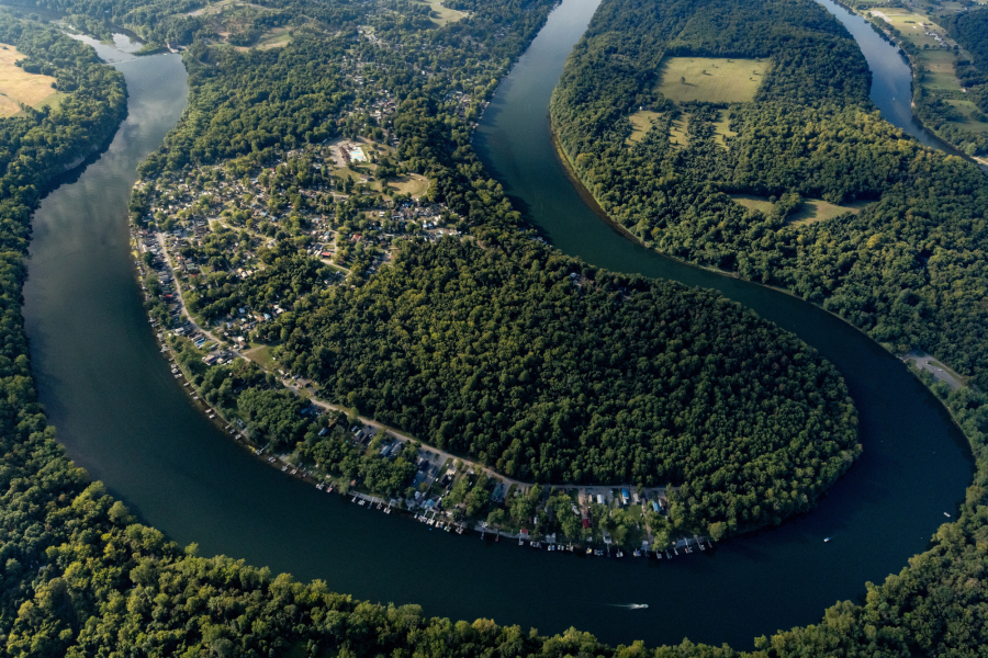 An aerial view of a horseshoe bend in a river bordered by forests and a small housing development.