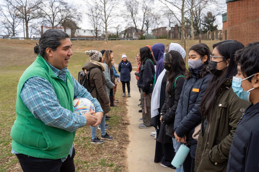 Abel Olivo stands with a soccer ball in hands talking to a group of students.