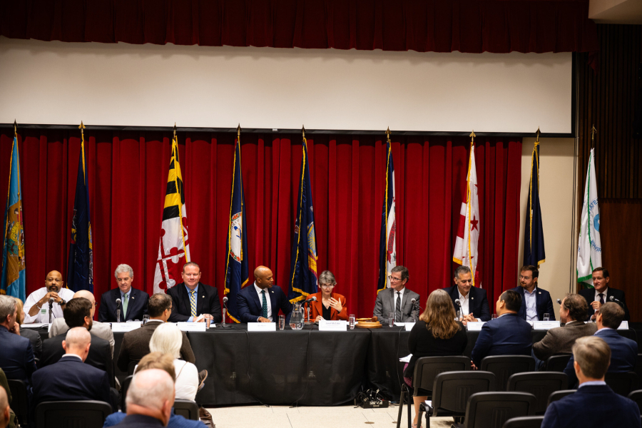 Members sit in front of flags and red cloth background.