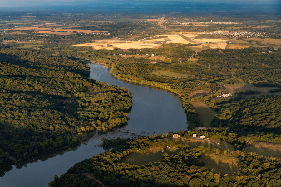 A photo taken from the air showing a winding river through trees and farm land in the distance.