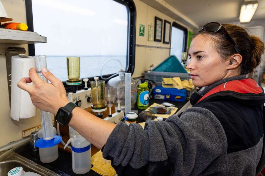 Woman in an enclosed section on a boat holds a beaker.