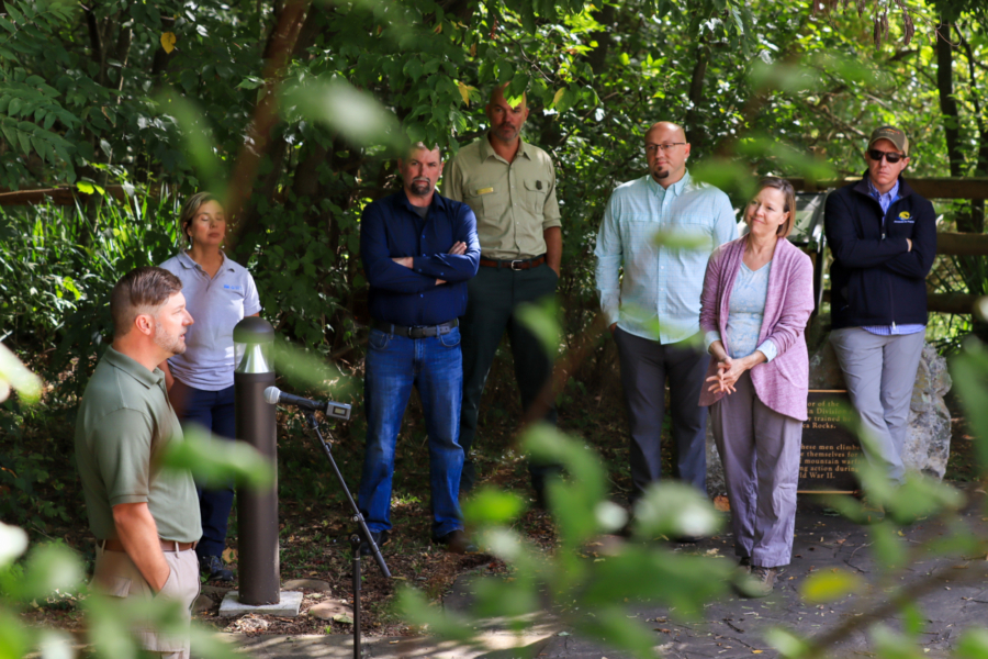 A group of people surrounded by trees listen to another person speak.