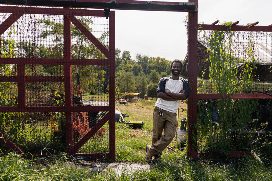 A farmer poses by red fencing on the farm.