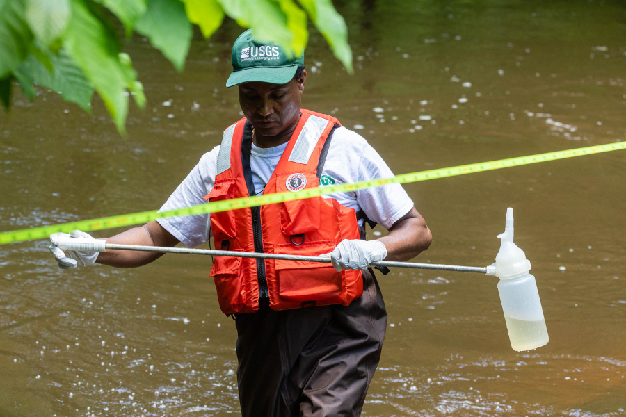 A man wades a river while collecting water quality samples.