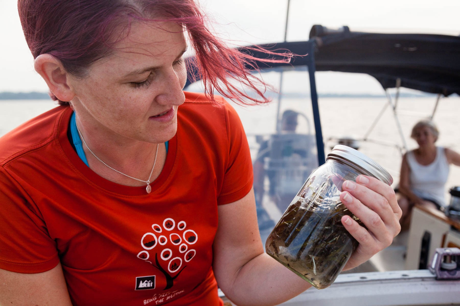 Julie is on a boat looking at a water sample in a jar.