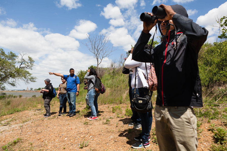 A group of students stands on a shoreline, using binoculars to look for wildlife.