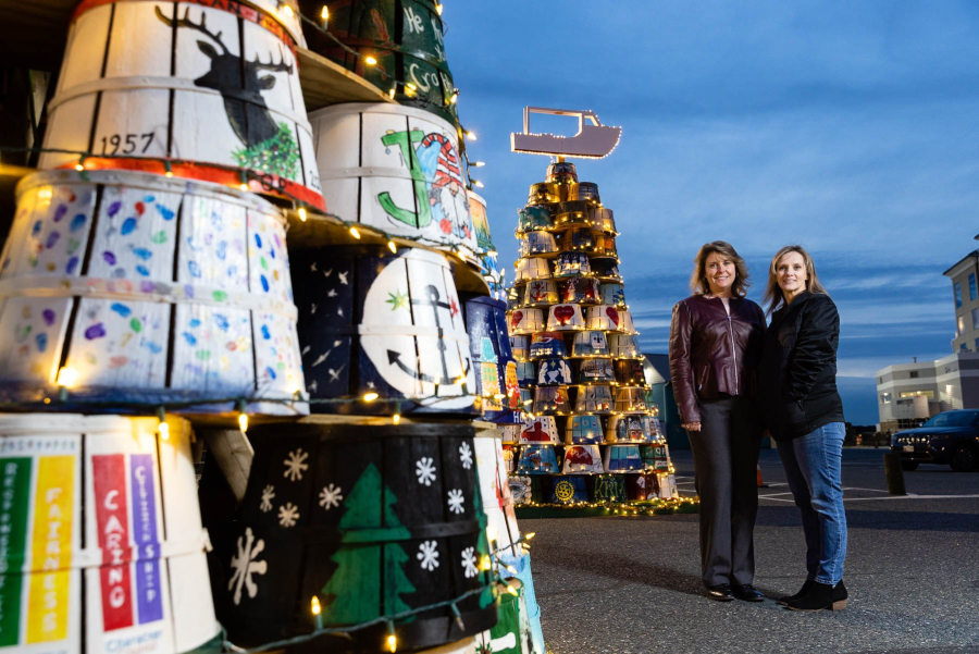 Two women pose by tree-shaped structures made up of crab baskets.