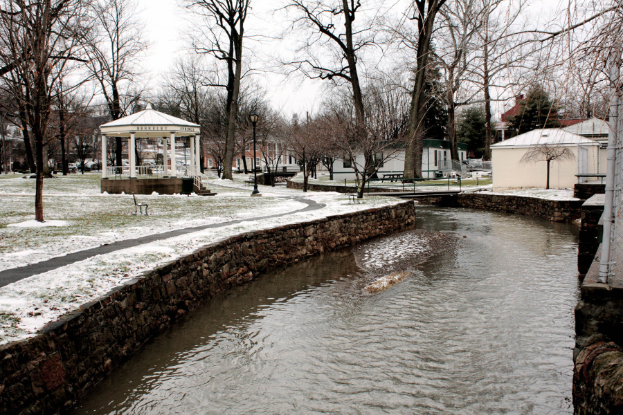 A photo of a stream flowing through a snowy garden with a gazebo.