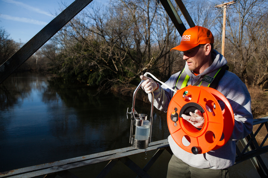 Researcher holds a device that he's about to lower into the water from a bridge.