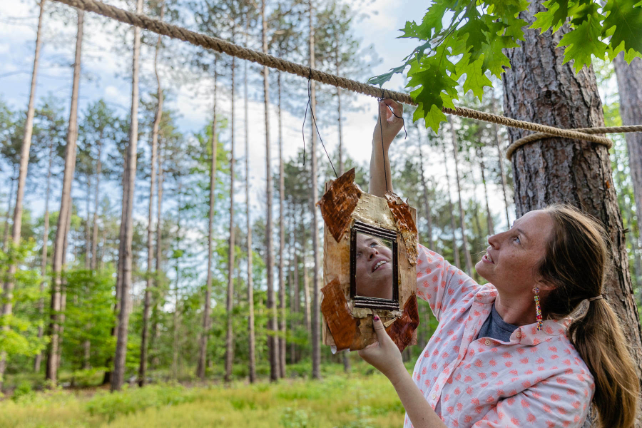 Woman hands a photo on a wooden pole strung between two trees.