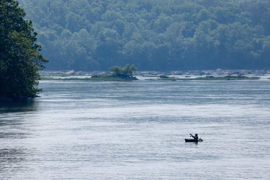 A far-off angler fishes from a kayak in the middle of the wide blue Susquehanna River.