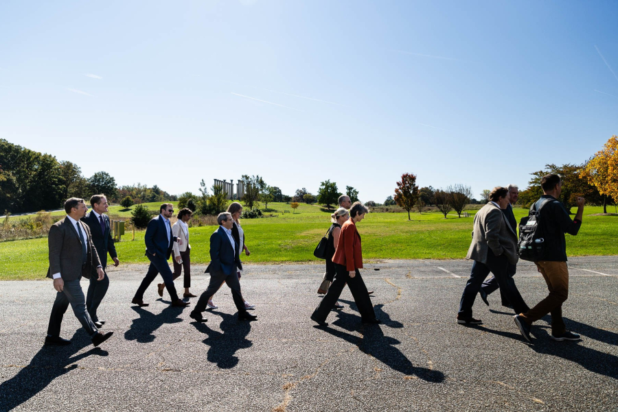 Several people walk in bright sunshine along a paved path, while the National Arboretum's National Capitol Columns stand tall in the distance.