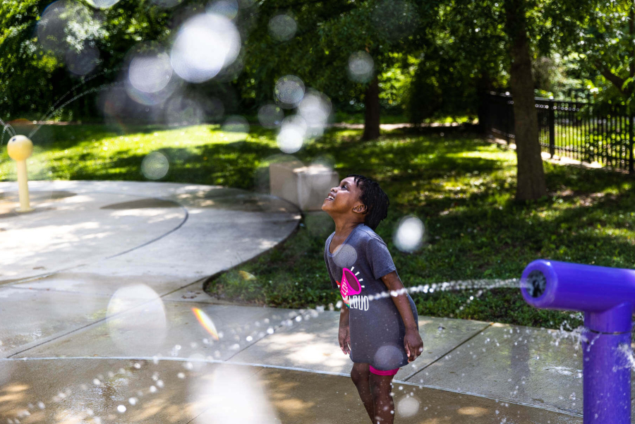 Little girl plays in a park where water is spraying.