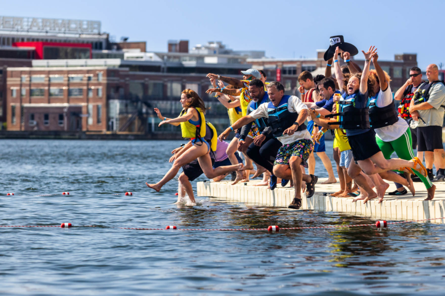 A group of people in life jackets and swim suits jump into Baltimore Harbor.