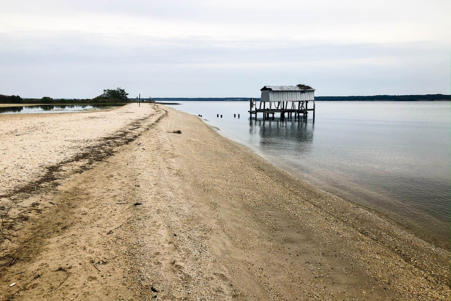 Beach with a small building on stilts in the water near the shore.