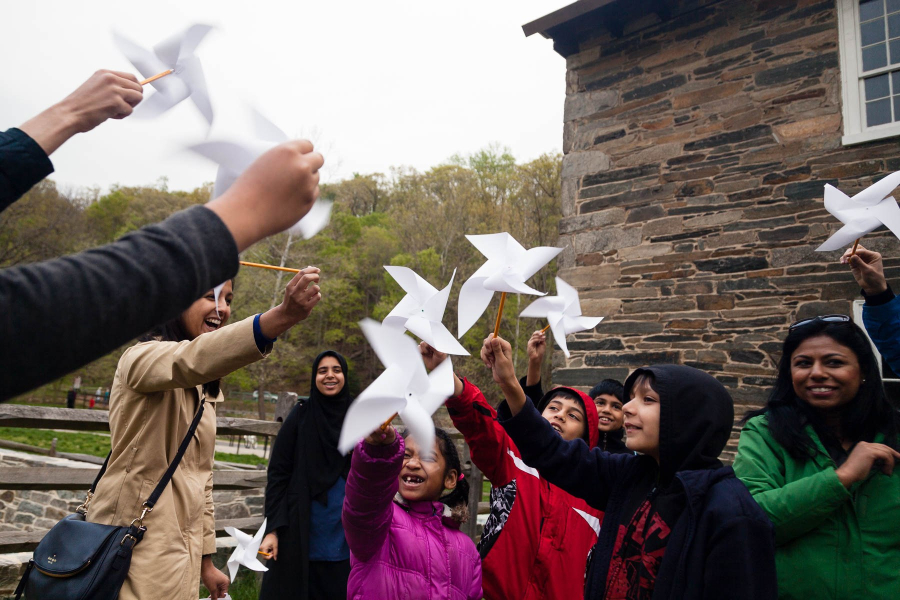 Children and adults raise paper pinwheels near the stone exterior of a historic mill.