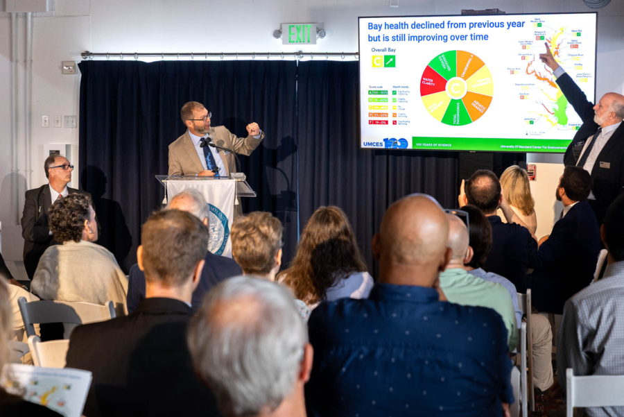 Two men stand on either side of a TV screen showing the report card.