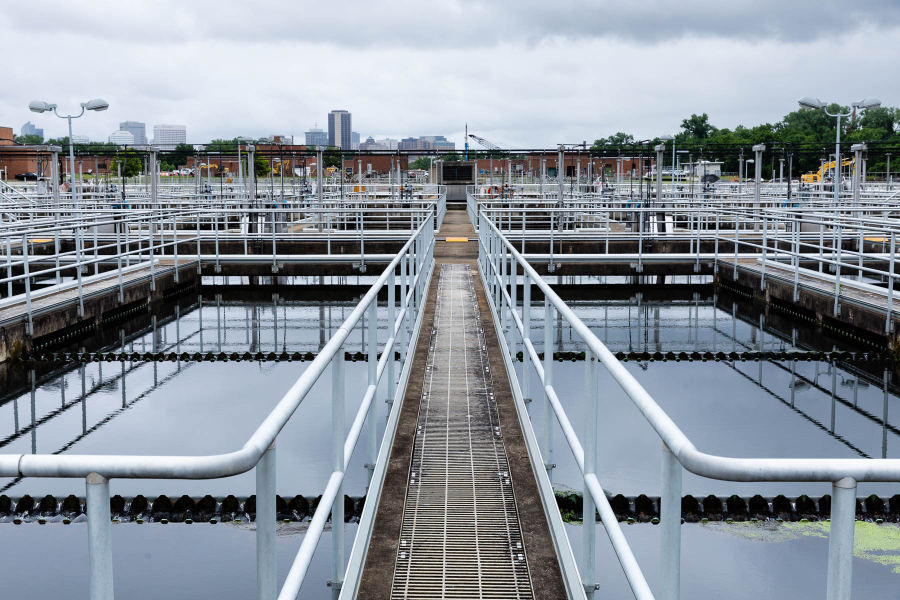 Rectangular pools of wastewater at a treatment plant reflect a cloudy sky with the city of Richmond on the horizon