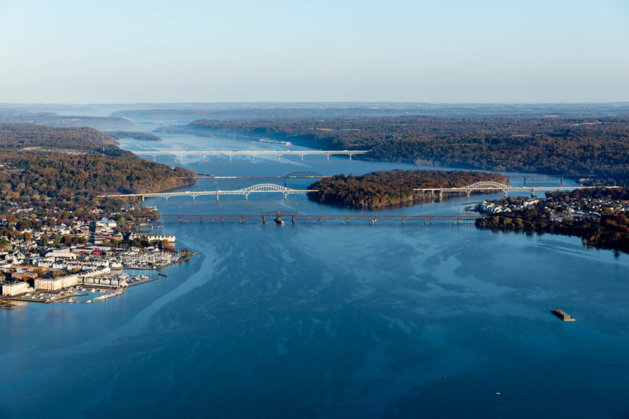 An aerial view of the Susquehanna River entering the Chesapeake Bay. Four bridges cross the river, much of the shoreline is forested, and a small riverfront town is visible on the left.