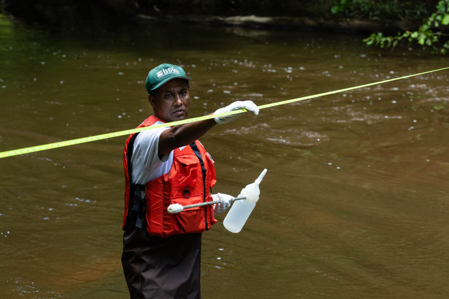 a man holds measuring tape steady as it stretches across a river.