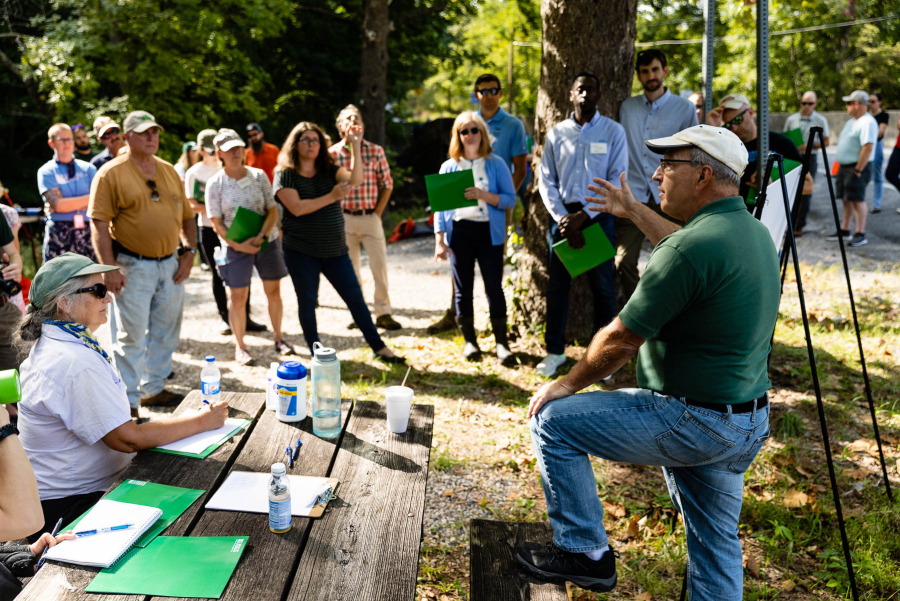 With a green shirt and white hat, Scott addresses a group gathered outside.