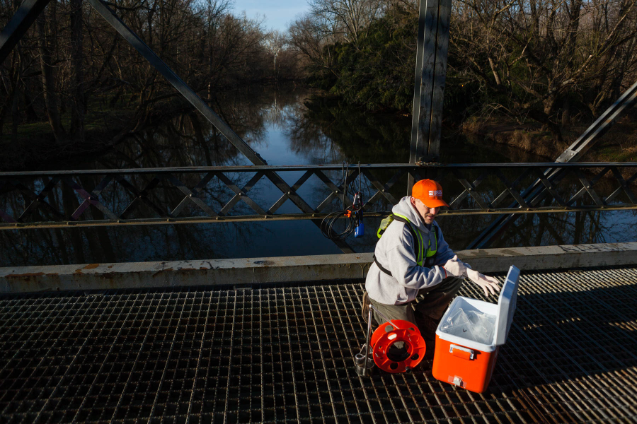 Man kneels by a bridge getting together equipment needed to monitor a river.