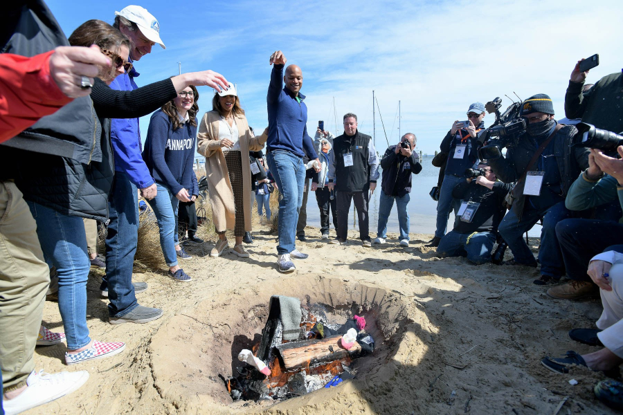 Governor Wes Moore throws a pair of socks into a fire pit on the Beach