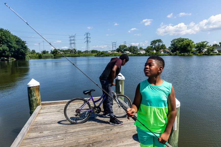 A kid hold a fishing pole and another is on a bike at a fishing pier.