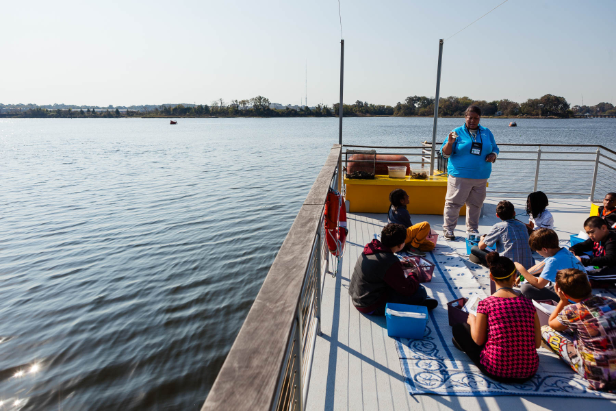 Students on a barge listen to an educator.